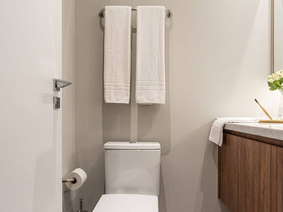 A modern bathroom with a toilet, a bidet, a towel rack with two towels, a wooden vanity, and a mirror.
