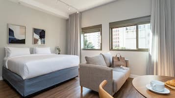 A hotel room with a bed, a sofa, a dining table, and two windows.