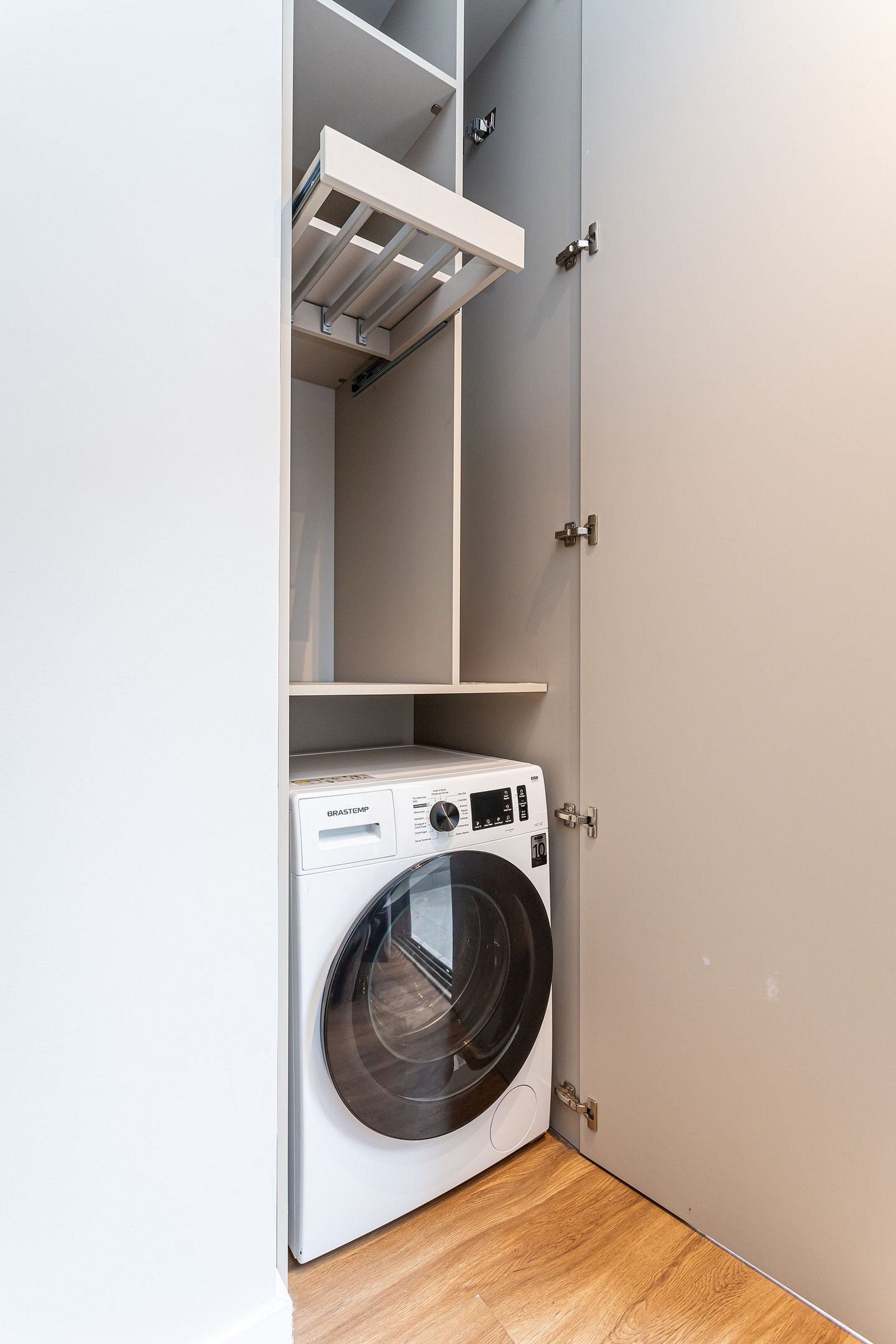 Une petite buanderie équipée d’un lave-linge à chargement frontal, d’une étagère au-dessus et d’une porte dotée d’une poignée.