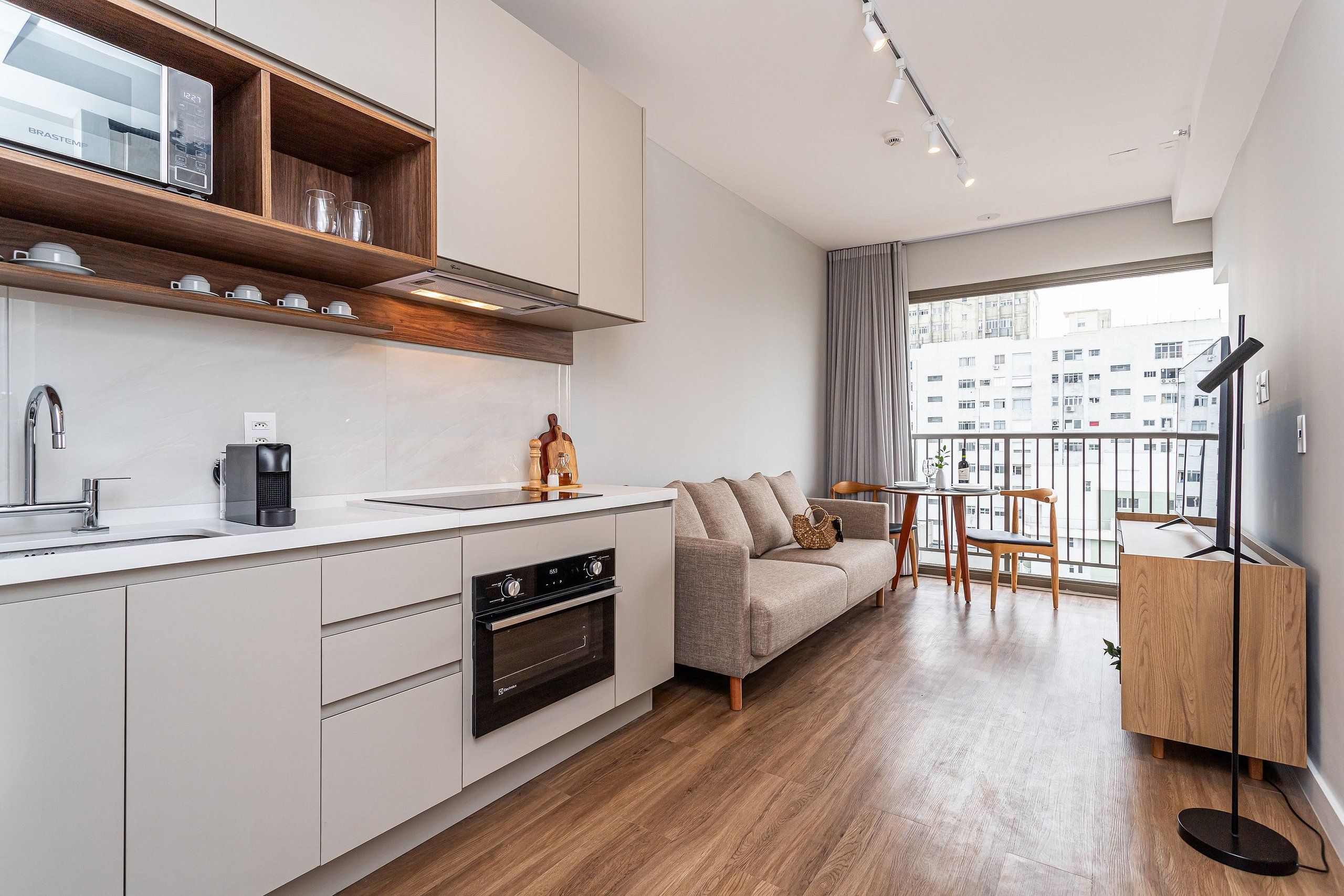 A modern kitchen with a built-in oven, a coffee machine, and a microwave. There is a dining area with a sofa and a table.