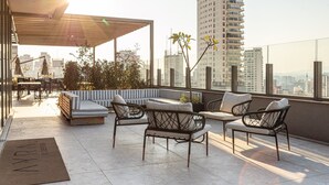 A rooftop terrace with seating, a pergola, and a city view.