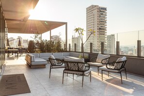 Una terraza en la azotea con mobiliario, una pérgola y vistas a la ciudad.