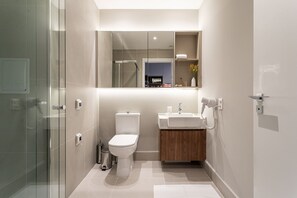 Un baño moderno con cabina de ducha de vidrio, inodoro, lavamanos y espejo sobre el lavamanos.