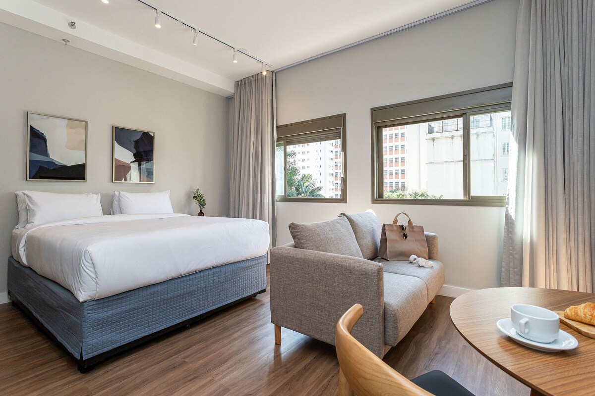 Une chambre d’hôtel avec un lit, un canapé, une table à manger et deux fenêtres.