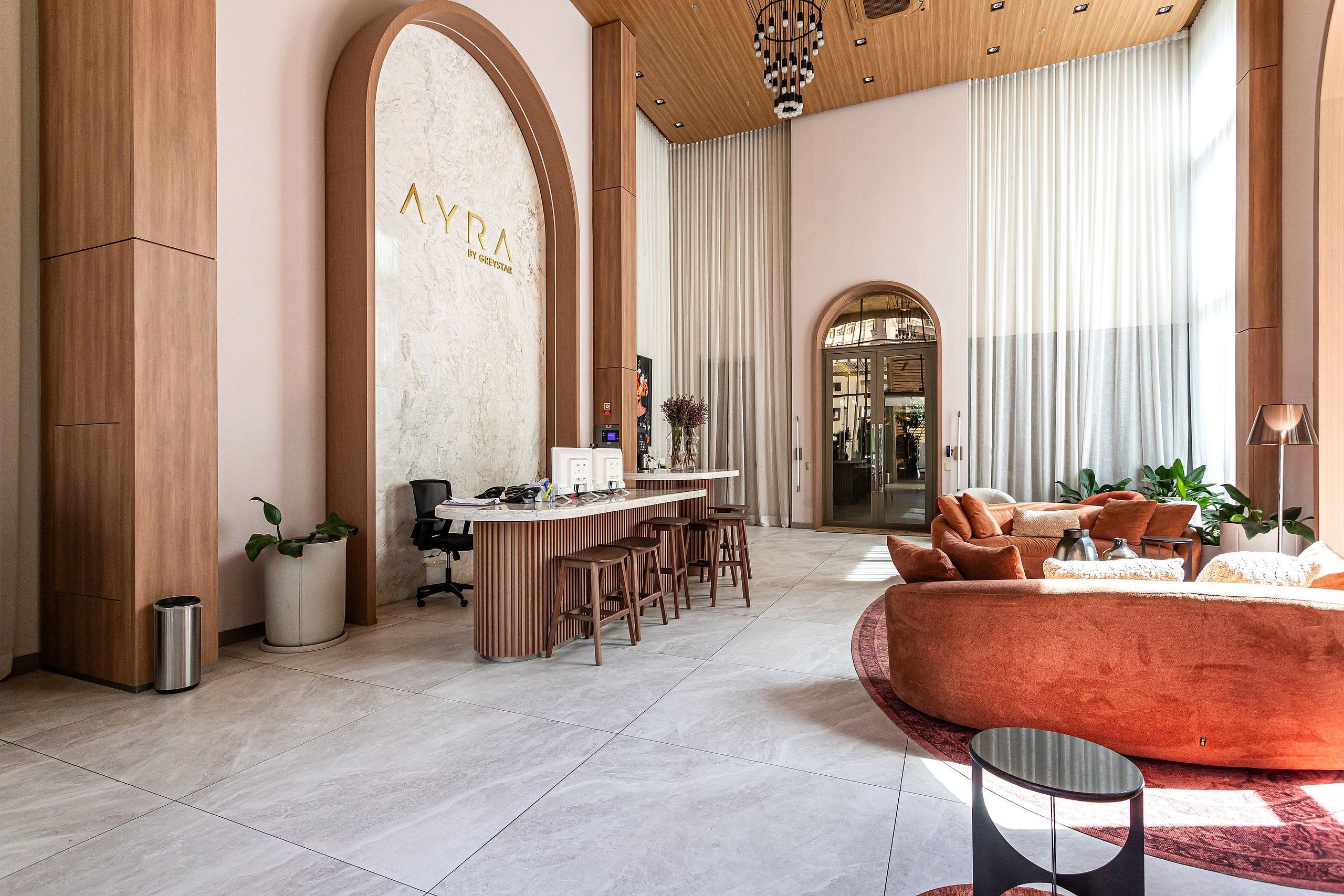 En modern hotellobby med en bar, en sittgrupp och en vägg av marmor där namnet ”AYRA” är inristat.