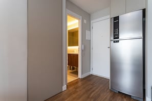 A modern kitchen with a stainless steel refrigerator, wooden flooring, and a visible bathroom with a mirror. - Apartamentos mobiliados com excelente vista e localização - Higienópolis (São Paulo)