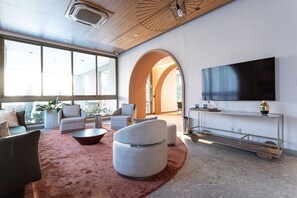 A modern living room with a large TV, comfortable seating, a coffee table, and a large window. - Apartamentos mobiliados com excelente vista e localização - Higienópolis (São Paulo)