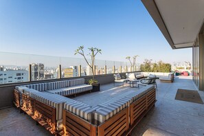 Une terrasse sur le toit avec un long banc en bois, une petite table et des chaises.