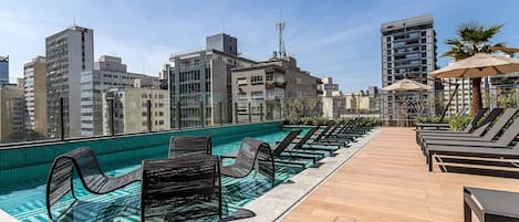 A rooftop pool area with lounge chairs and a wooden deck.