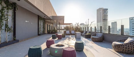 A rooftop terrace with outdoor seating, a view of the city, and a modern building facade.