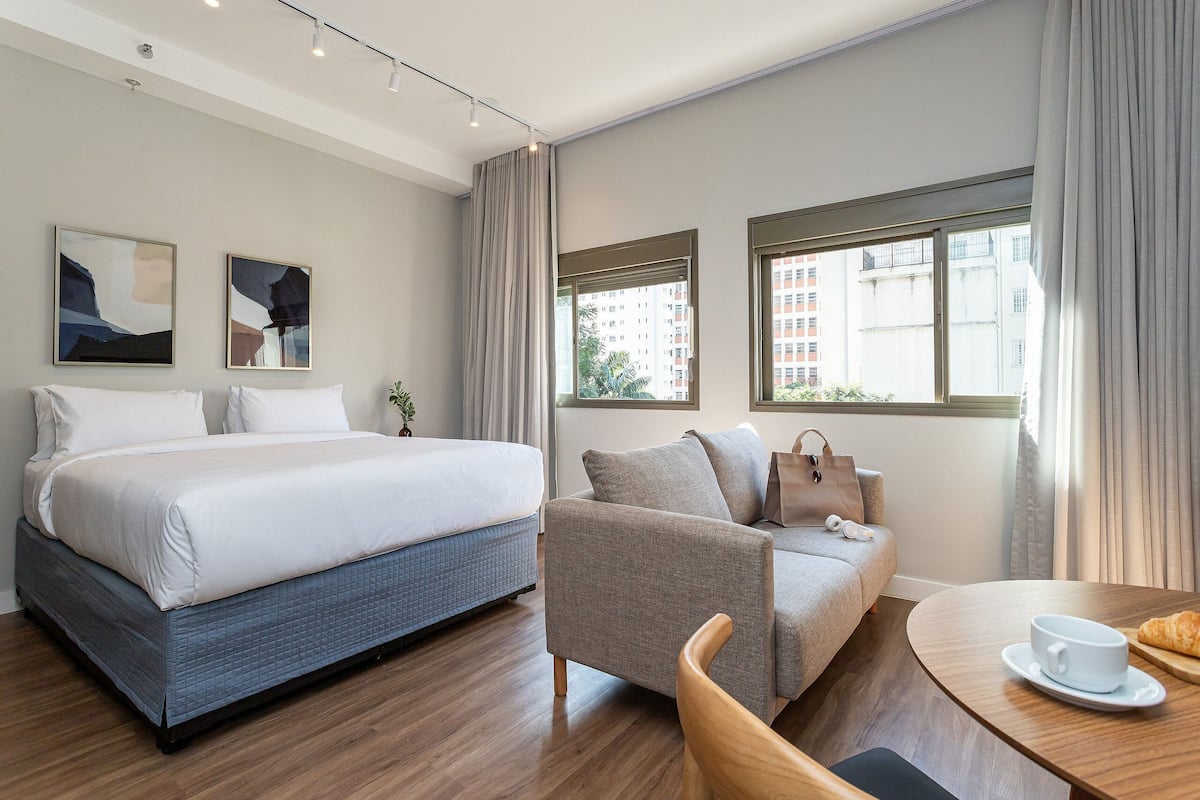 Une chambre d’hôtel avec un lit, un canapé, une table à manger et deux fenêtres.