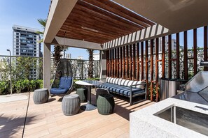 A rooftop patio with a wooden pergola, outdoor seating, and a grill area.