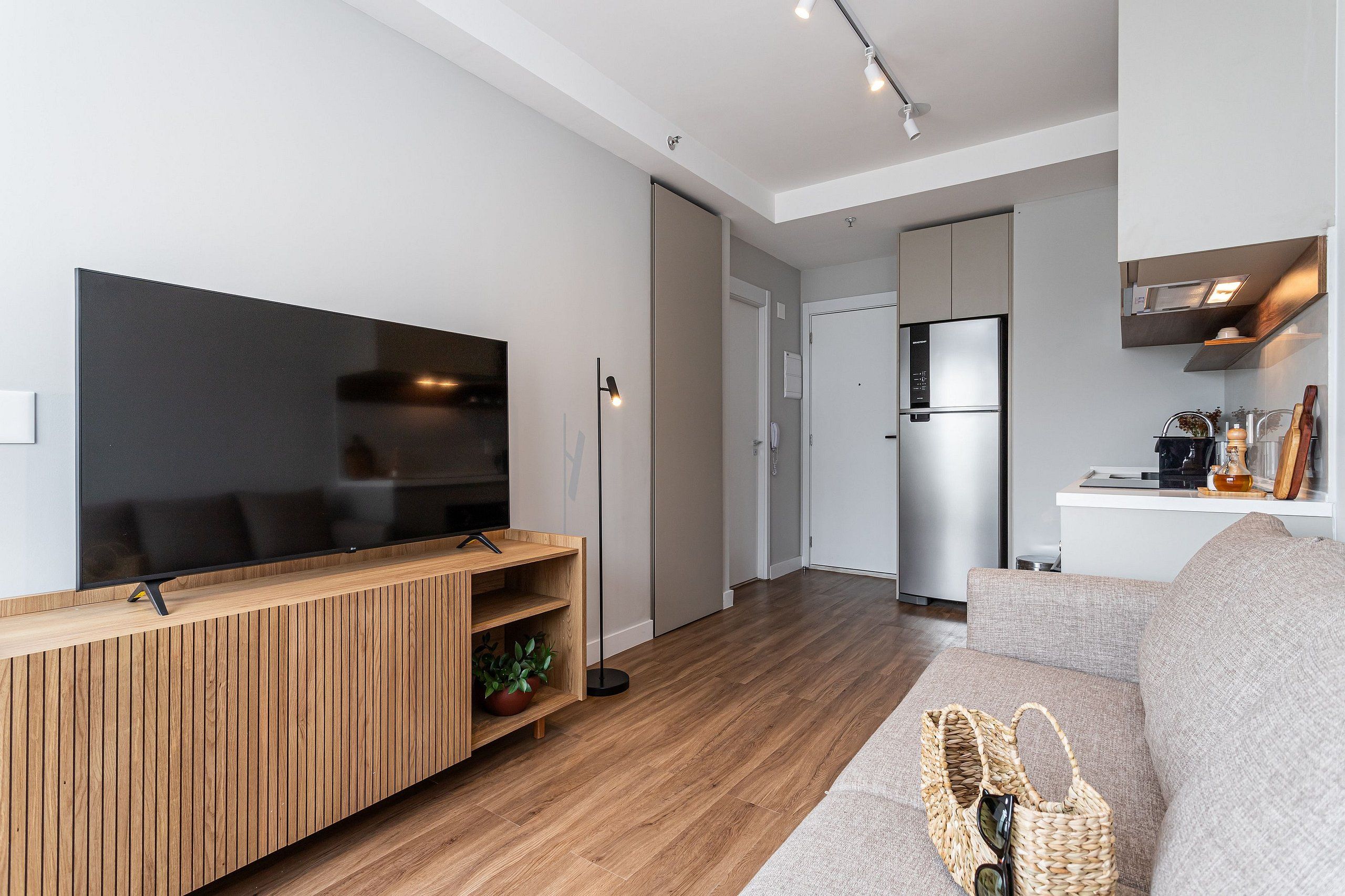 A modern living room with a flat-screen TV, wooden entertainment unit, and a grey sofa.