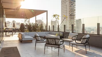 Una terraza en la azotea con mobiliario, una pérgola y vistas a la ciudad.
