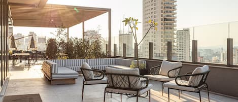 A rooftop terrace with seating, a pergola, and a city view.