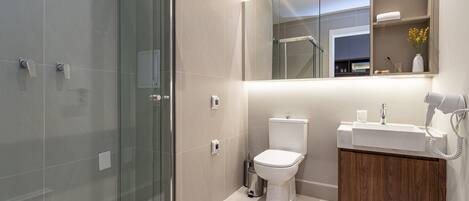 A modern bathroom with a glass shower enclosure, a white toilet, and a vanity with a mirror and towel rack.