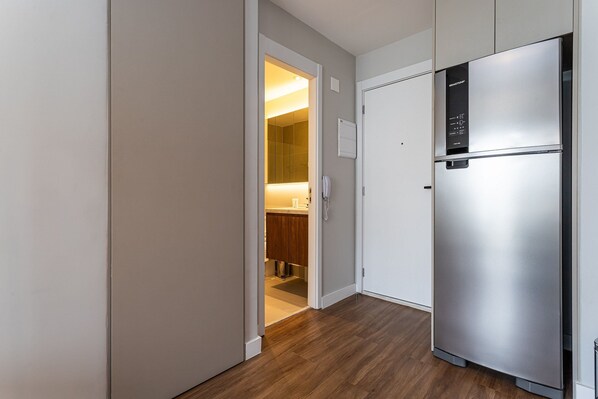 A modern kitchen with a stainless steel refrigerator, wooden flooring, and a visible bathroom with a mirror. - Apartamentos mobiliados com excelente vista e localização - Higienópolis (São Paulo)