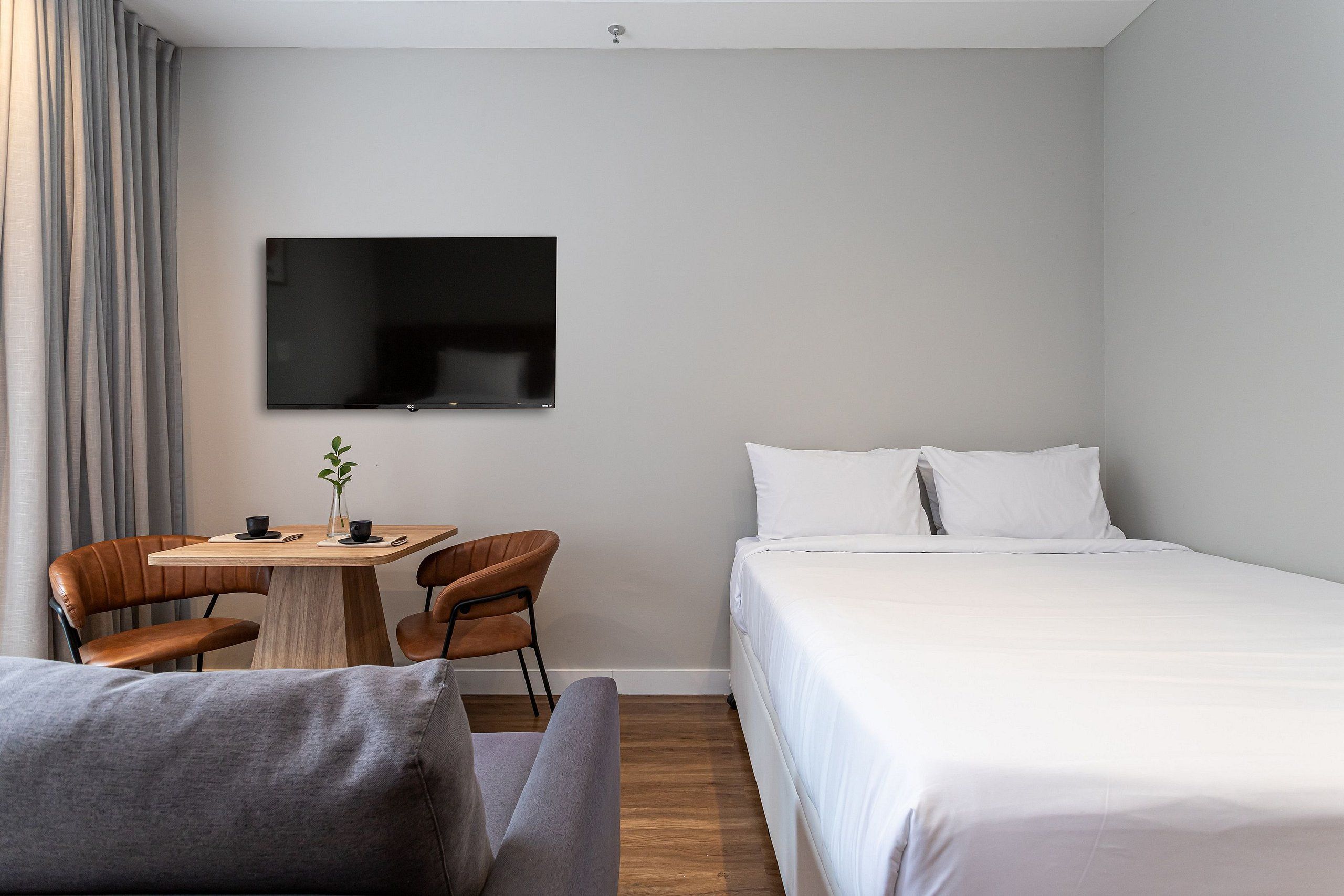 A hotel room with a bed, a TV mounted on the wall, a small table with chairs, and a sofa.