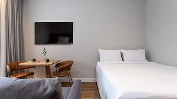 Et hotelværelse med seng, fjernsyn ophængt på væggen, et lille bord med stole og en sofa.