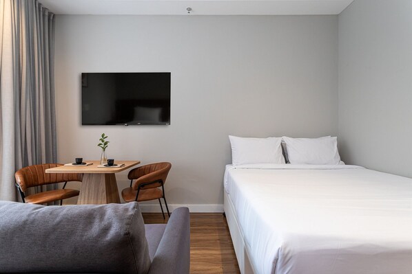 A hotel room with a bed, a TV mounted on the wall, a small table with chairs, and a sofa.