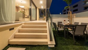 Een modern buiten terras met een eettafel en stoelen, een trap naar een hoger niveau en een glazen deuropgang.