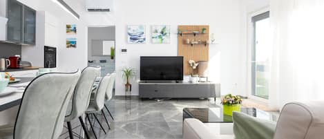 A modern living room with a flat-screen TV, a dining area with chairs, a sofa, and a coffee table.