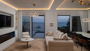 A modern living room with a TV, sofa, dining area, and large windows overlooking a body of water.