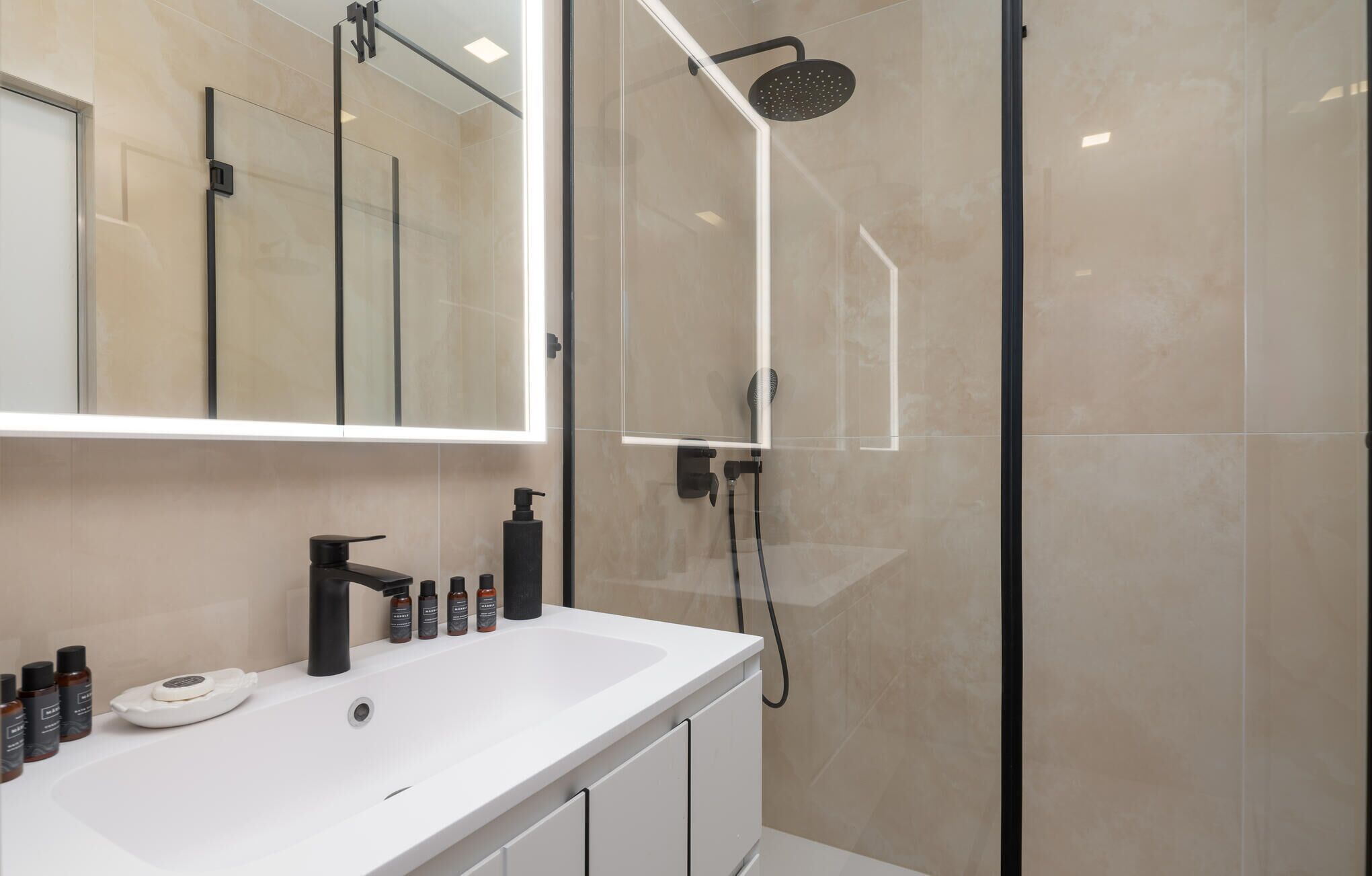 A modern bathroom with a glass-enclosed shower, a large mirror, and a white sink with toiletries.