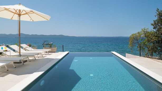 An infinity pool with a clear view of the sea and mountains in the background.
