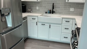 A modern kitchen with white cabinets, a stainless steel refrigerator, a built-in oven, and a gray-tiled backsplash.