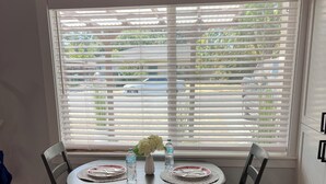 A dining area with a round table, four chairs, and a window with blinds.