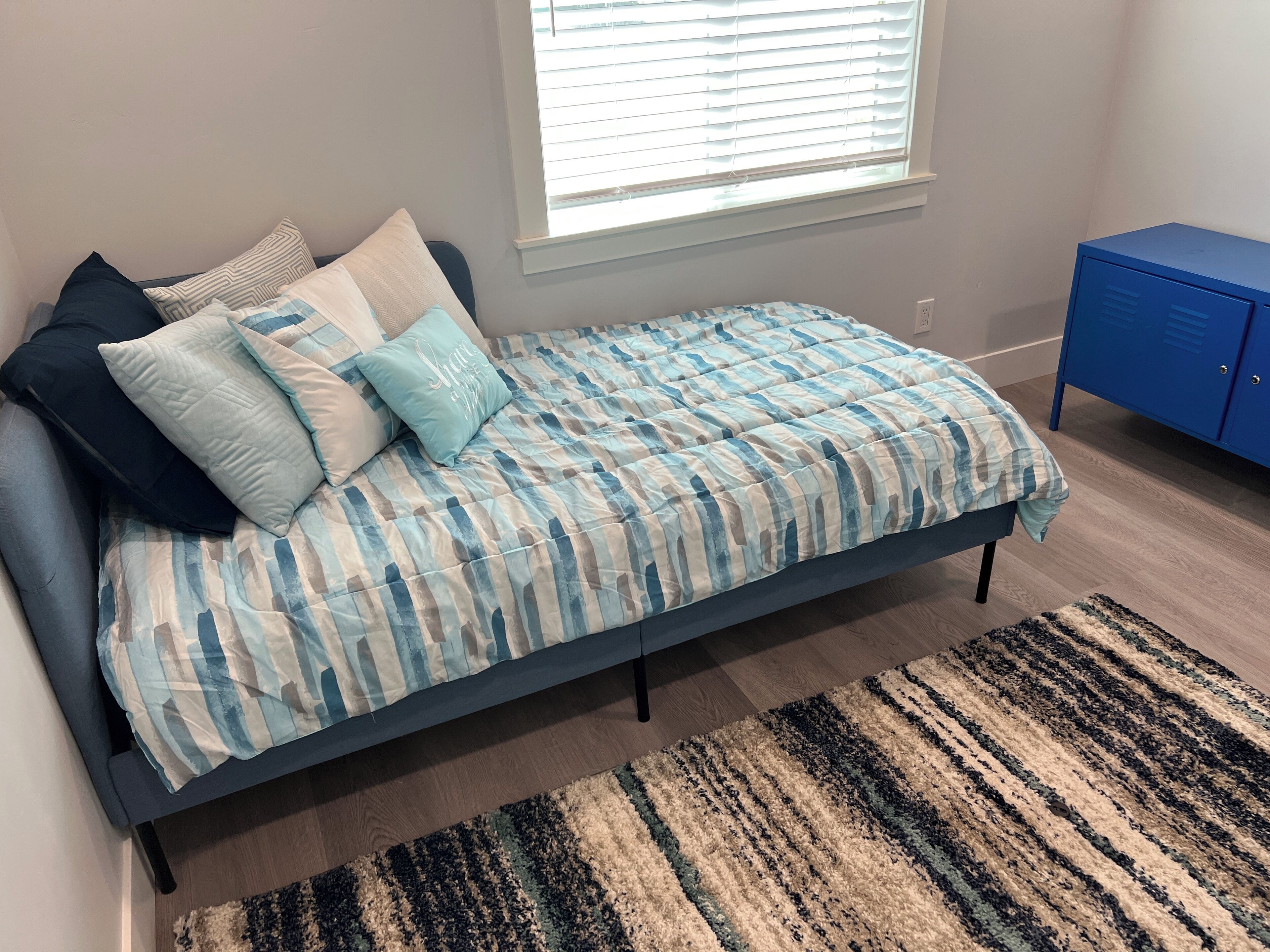 Ein Schlafzimmer mit einem Bett, einem blauen Kleiderschrank und einem Fenster mit Jalousien.