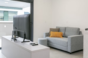 Una sala de estar moderna con un sofá gris, una mesa de centro blanca y un televisor de pantalla plana sobre un mueble.