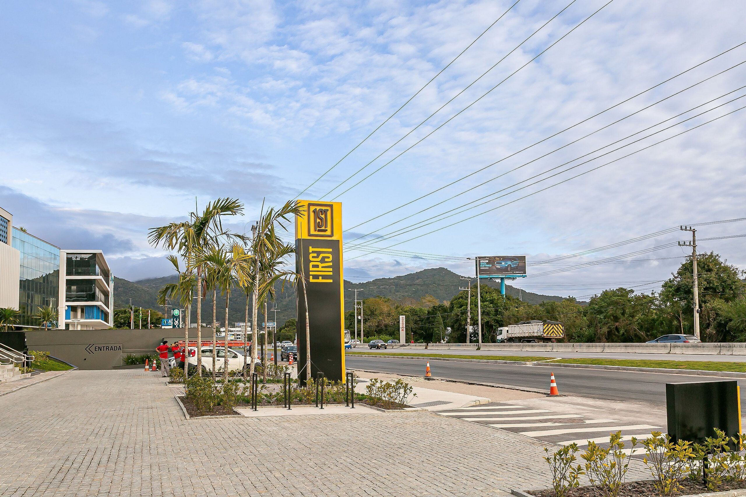 A paved entrance area with a sign indicating the first floor, a modern building, and a road with vehicles.