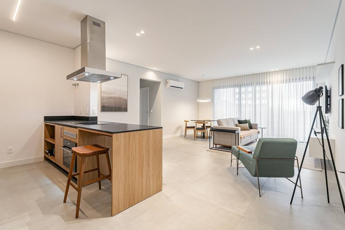 Une cuisine moderne dotée d’un îlot central, un coin repas avec une table et des chaises, et un salon avec un canapé et une lampe.
