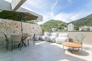 Um pátio externo com paredes de pedra, uma mesa, cadeiras, um sofá e um guarda-sol.