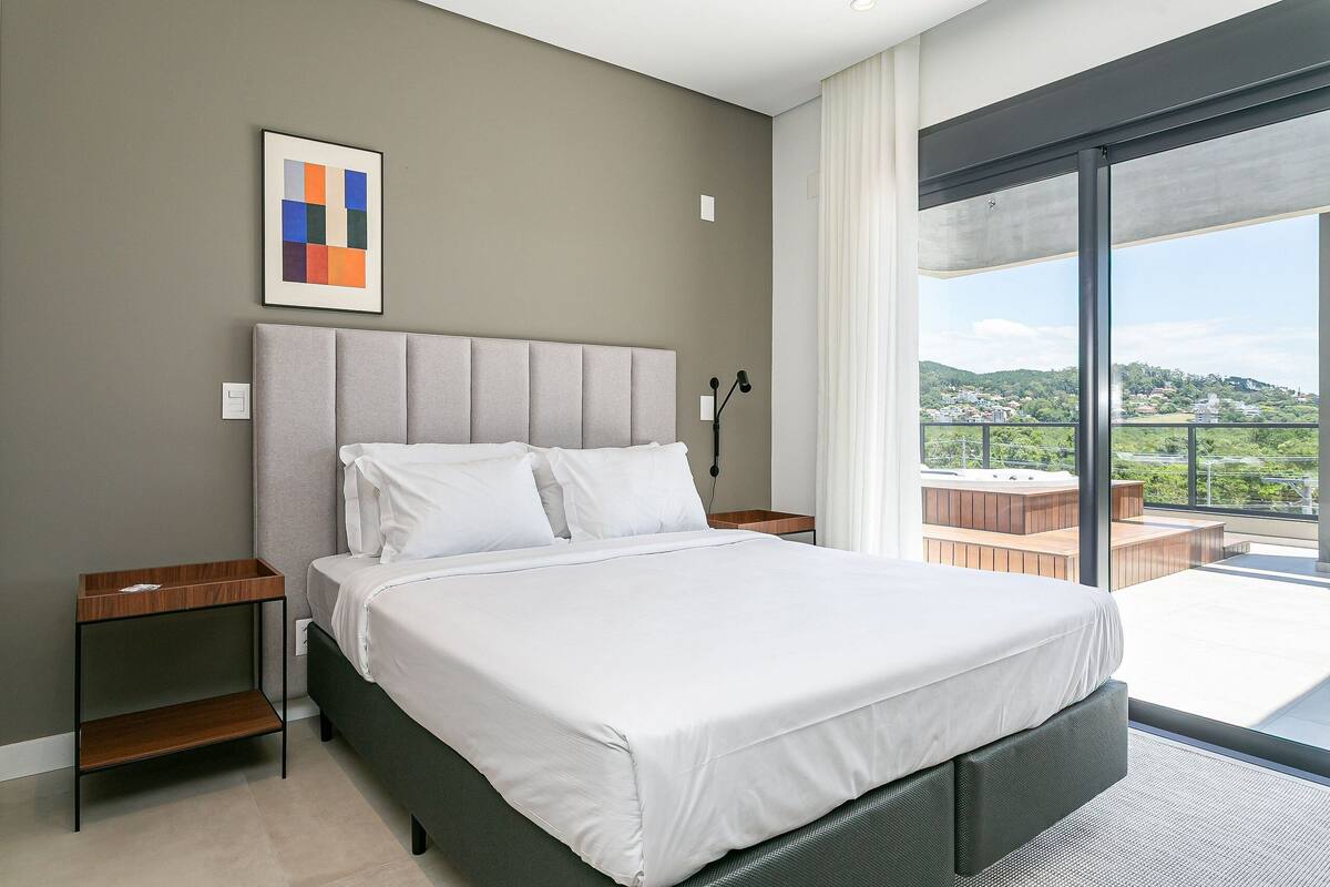 Une chambre moderne avec un grand lit, une table de chevet, une commode et une vue sur un balcon doté d’un jacuzzi.