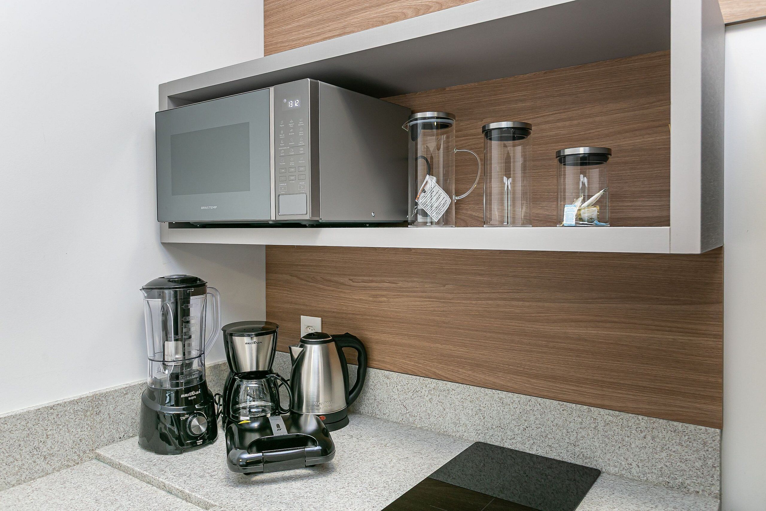 Una cocina con microondas, licuadora, cafetera y recipientes de vidrio sobre una encimera.
