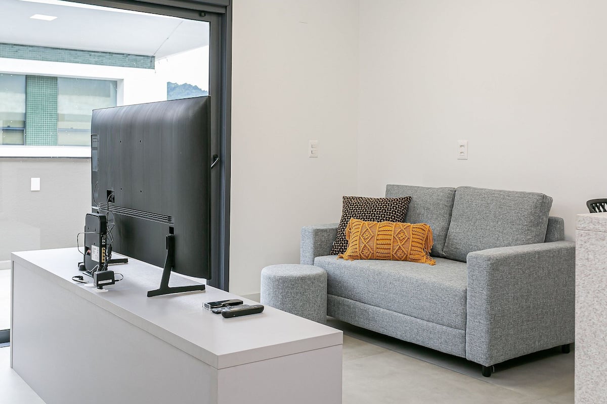 Un salon moderne avec un canapé gris, une table basse blanche et un téléviseur à écran plat posé sur un meuble.