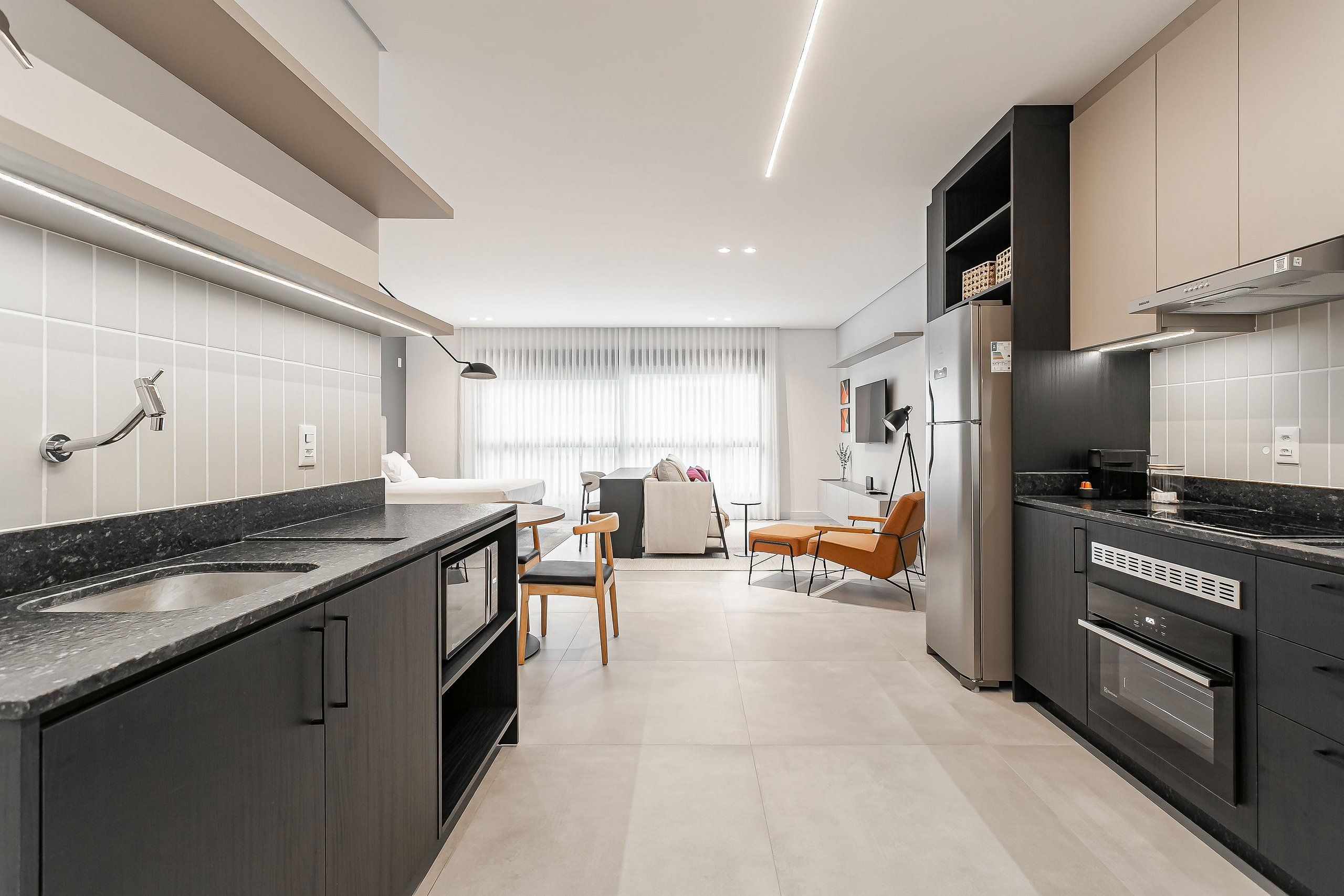 A modern kitchen with dark cabinetry, a large island, and a dining area with a sofa and chairs.