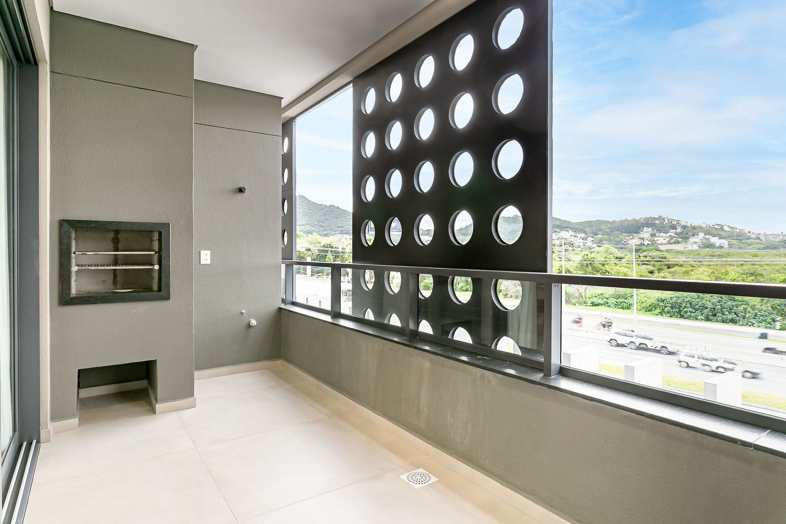 A balcony with a view of a road and hills, a metal grill, and a small ventilation grate.