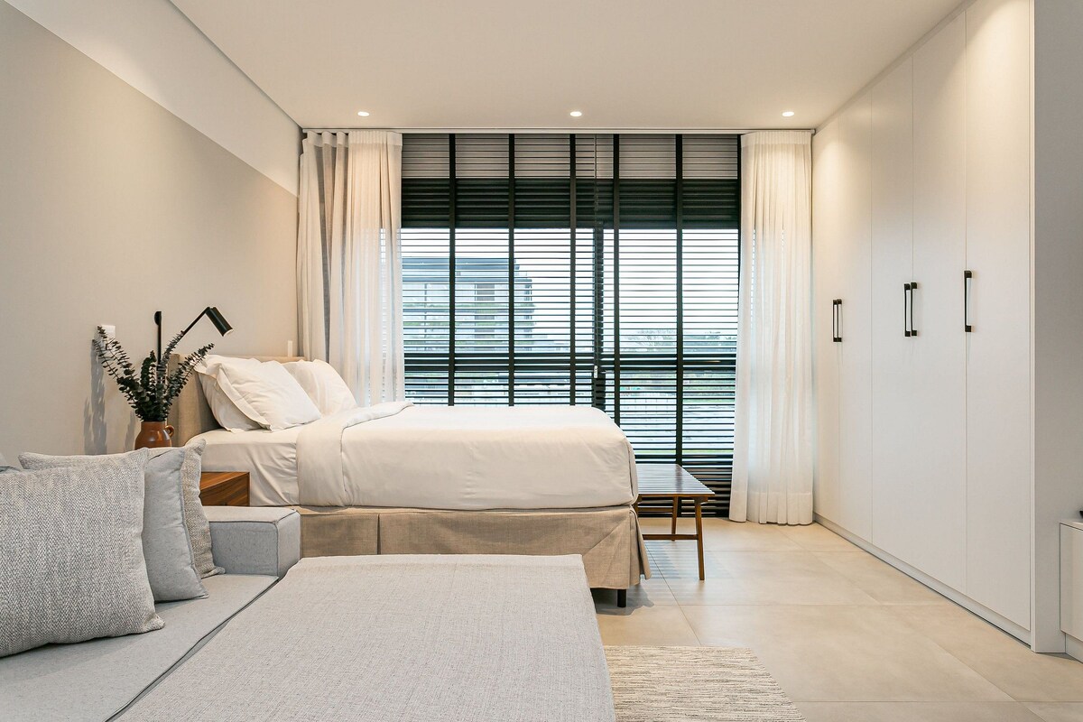 A modern bedroom with a bed, bedside tables, a sofa, and a wardrobe.