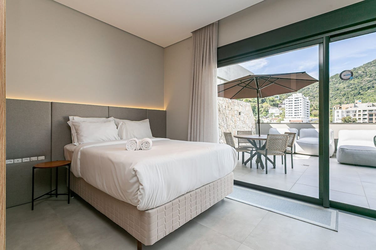Une chambre d’hôtel moderne avec un grand lit, une petite table et un balcon doté d’un espace salon extérieur.