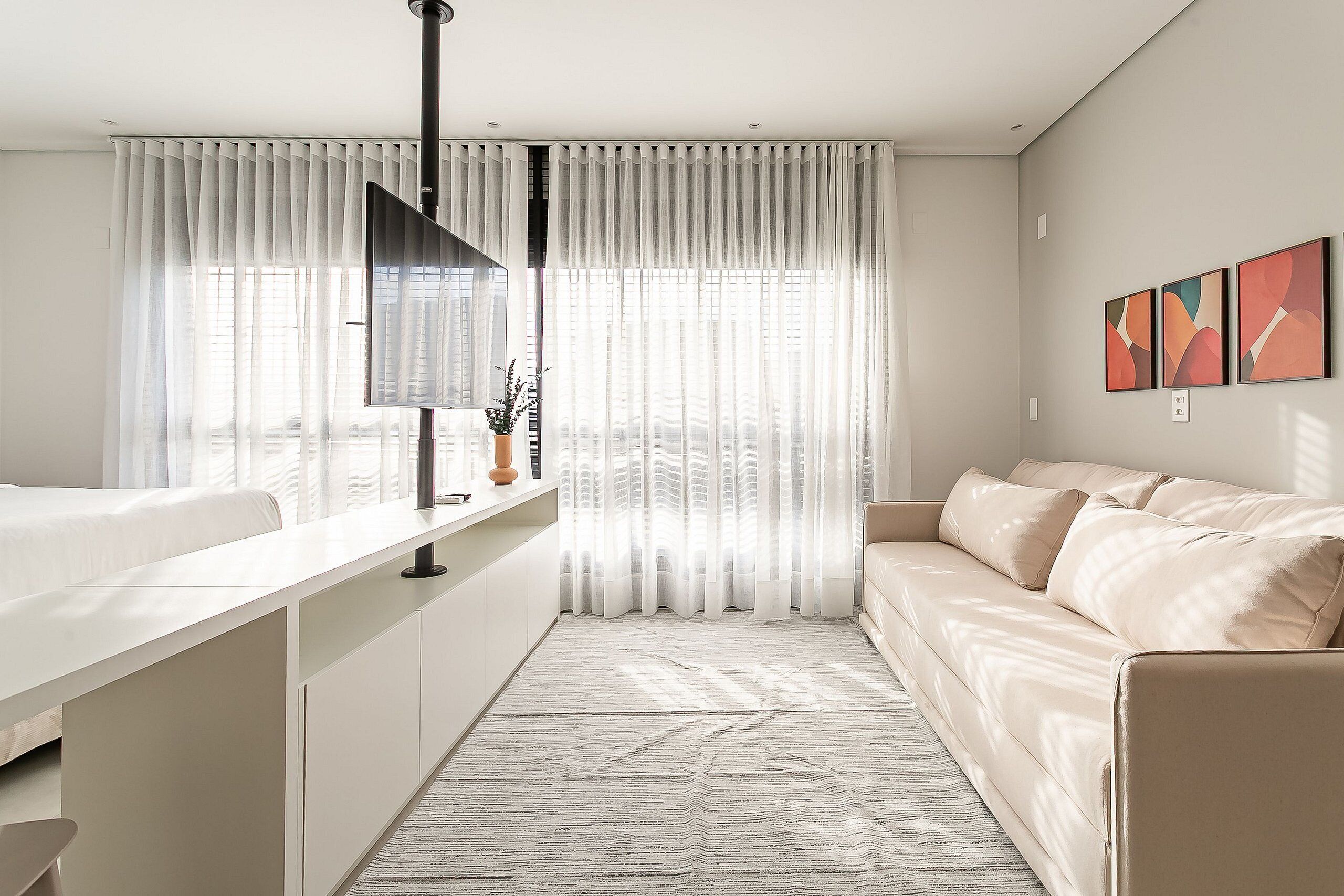 Une chambre moderne comprenant un lit, une table de chevet, des rideaux, un canapé et des œuvres d’art abstraites accrochées au mur.