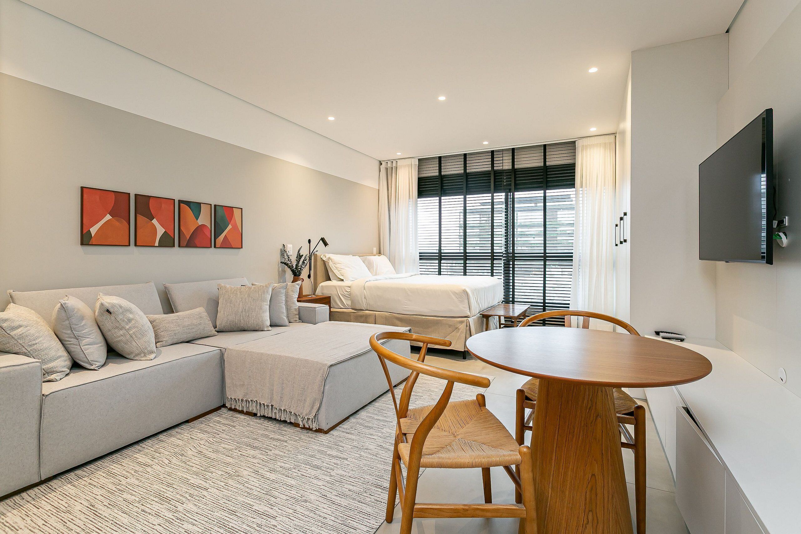 Quarto de hotel moderno com sofá, cama, mesa de jantar e televisão.