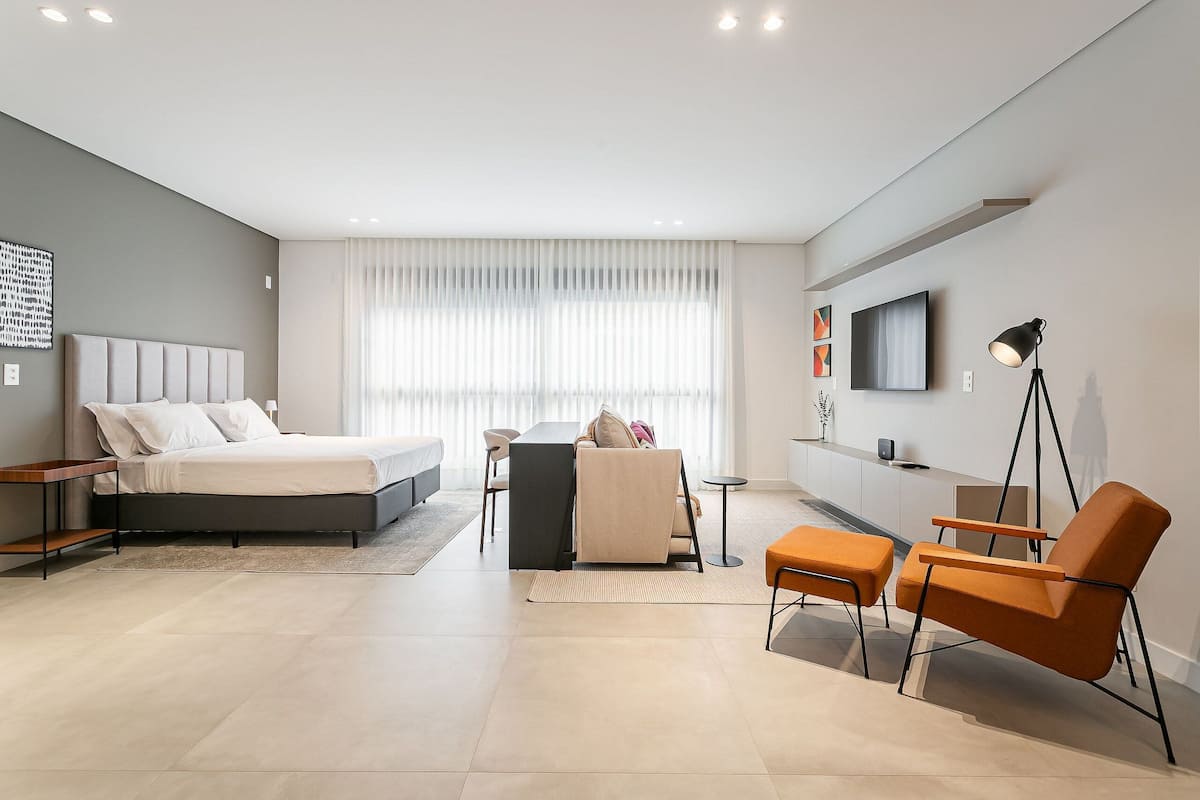 Une chambre à coucher moderne avec un lit, un canapé, un fauteuil et un téléviseur fixé au mur.