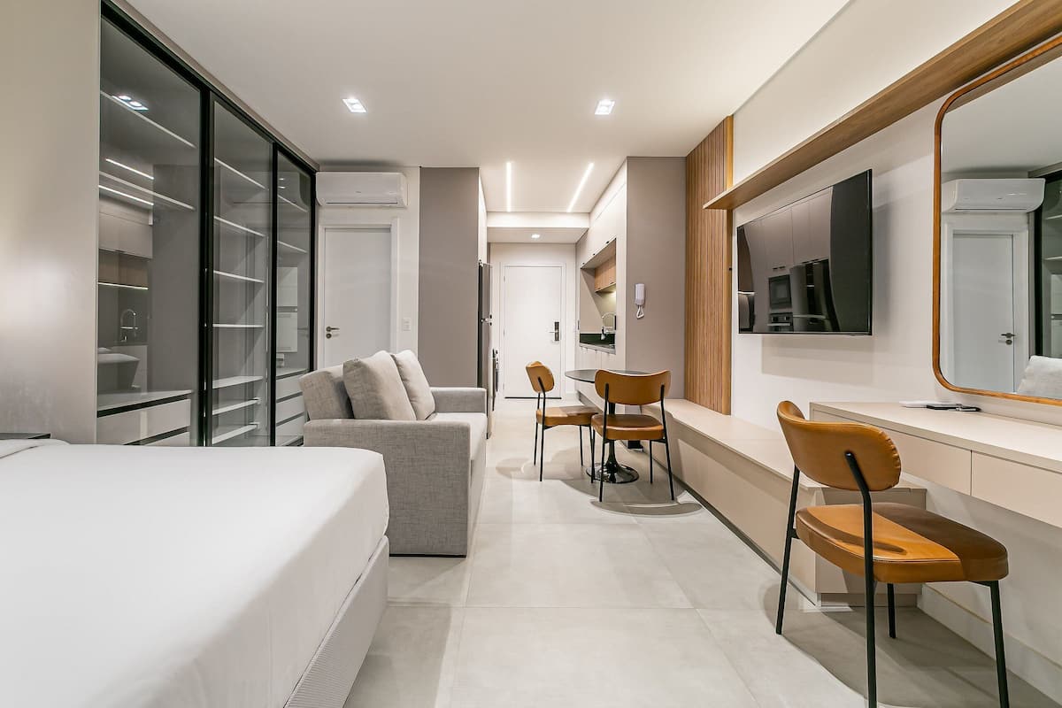 Une chambre d’hôtel moderne équipée d’un lit, d’un canapé, d’un coin repas avec des chaises, d’une télévision et d’un grand miroir.