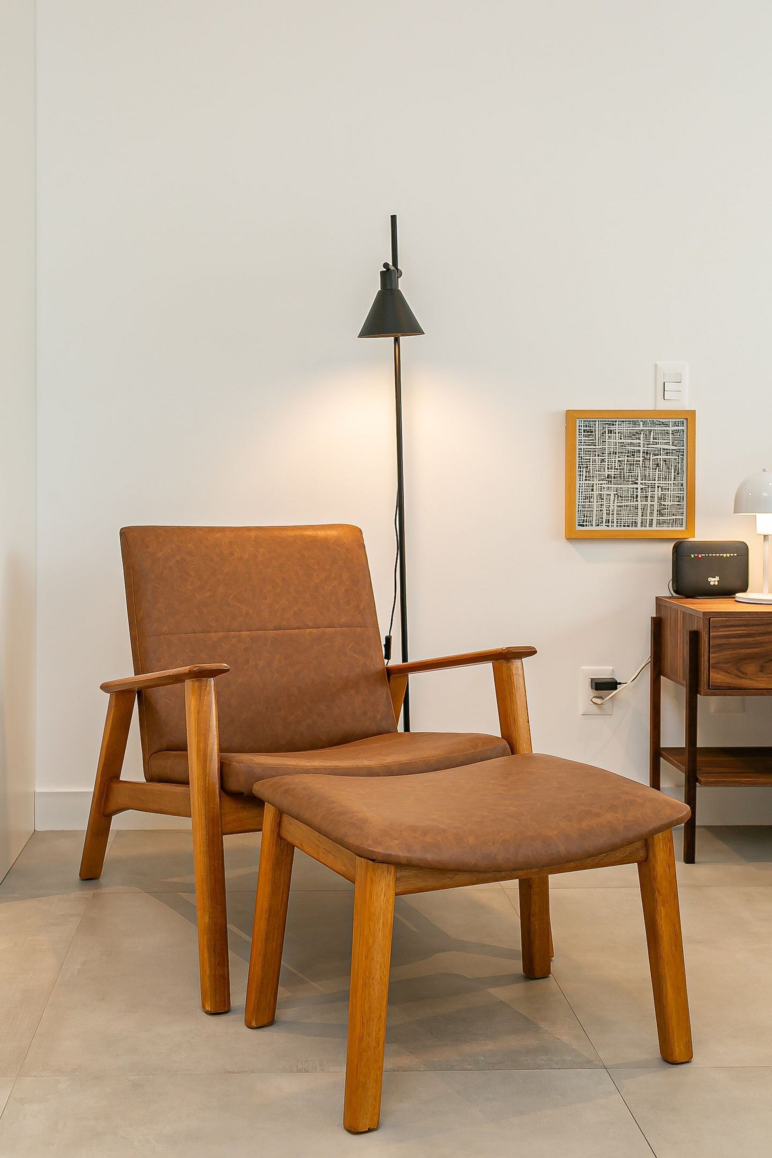 En modern stol med träben och en vadderad sits, en golvlampa, ett litet bord med en radio och ett inramat, abstrakt konstverk på väggen.
