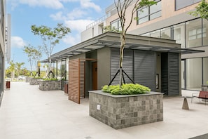 Un edificio moderno con un espacio exterior cubierto, macetas con plantas y una zona de estar.