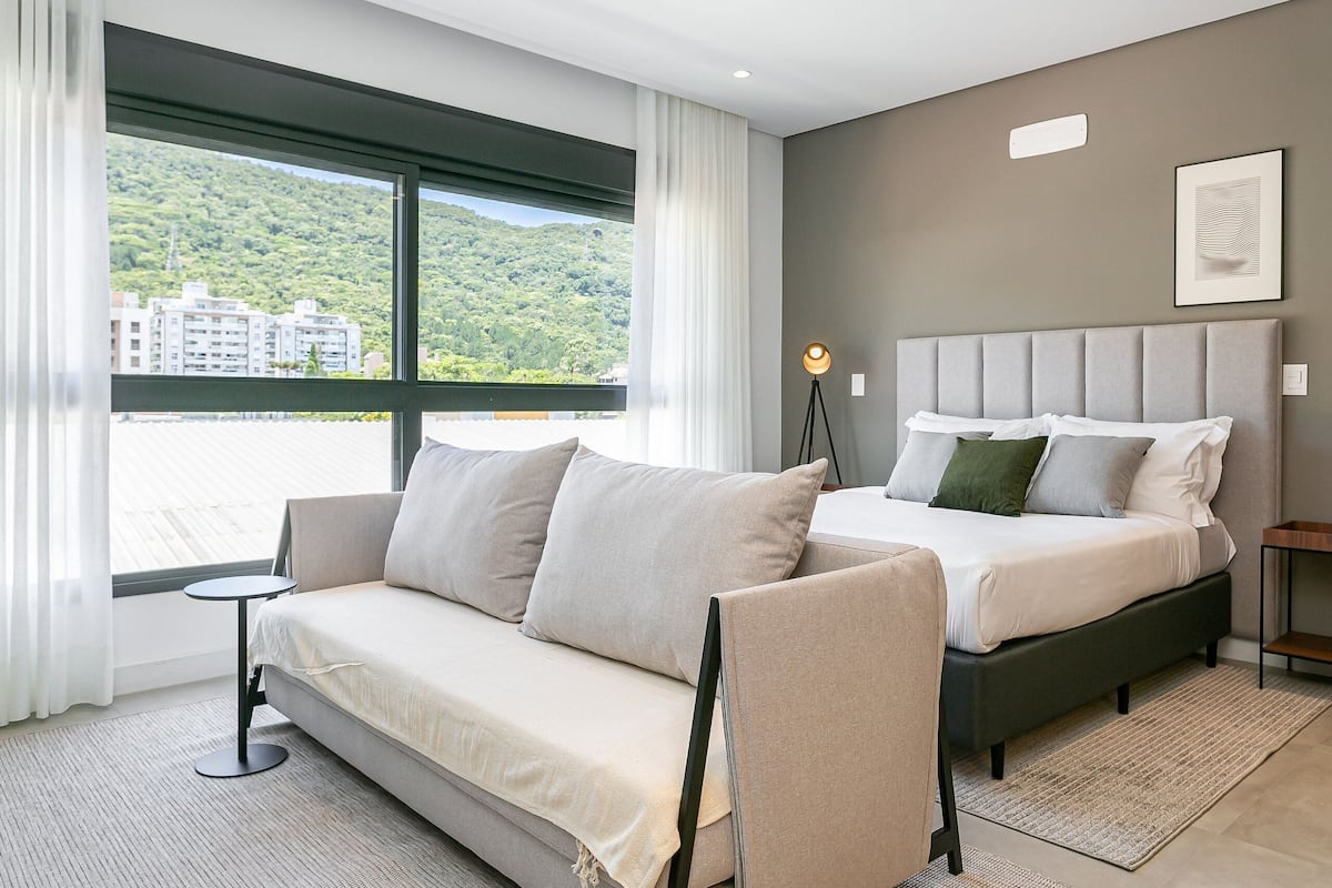 Une chambre moderne avec un canapé, un lit, une petite table et une vue sur une colline verdoyante.